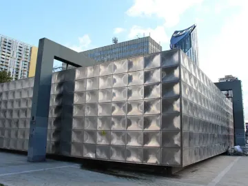 Michael Faraday Memorial with reflective stainless steel panels and dark support beams against a blue sky.