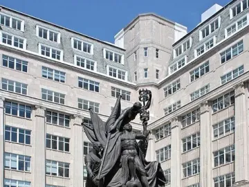 Nelson Monument in Liverpool with bronze figures on a stone base beside a tall stone building.