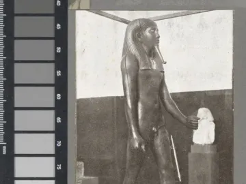 Standing statue of King Hor with a headdress and broad collar, shown stepping forward on a rectangular base.