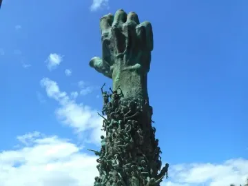 The Miami Beach Holocaust Memorial features a towering bronze hand rising above clustered human figures and scattered sculptures in a plaza.
