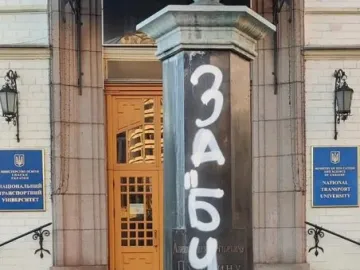 Graffiti-covered pedestal of the Pushkin Bust with a decorative cap at the top, standing before a building entrance.