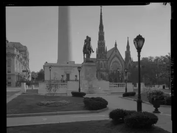 Lafayette Monument with a dark equestrian statue on a stone pedestal, a tall cylindrical monument behind it, and churches and buildings around the plaza.