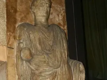 Scior Carera, a weathered stone statue of a draped standing man holding a spherical object, on an inscribed plinth.