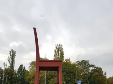 Broken Chair sculpture with a tall backrest and one broken leg on a paved plaza, with pedestrians and a bus in the background.