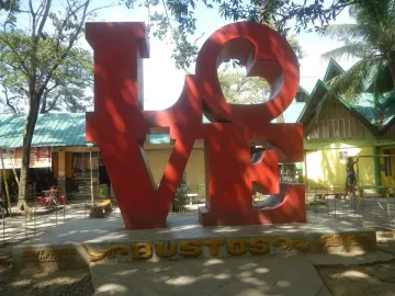 Bright red LOVE sculpture with a tilted O on a concrete base in Bustos, Bulacan.