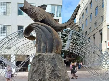 The Chicharro sculpture, a dark fish mounted on a tall stone pillar, stands in a plaza surrounded by red and yellow poinsettias.