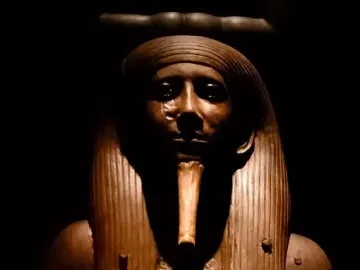 Upper body of the Ka statue of King Hor with a striped headdress and false beard against a dark background.