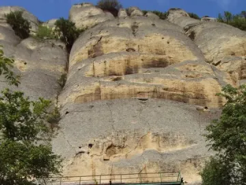 Rock face partly hidden by trees with a metal observation platform on the Madara Rider cliff.