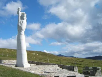 Our Lady of the Isles statue on a tiered stone platform in a grassy landscape with hills behind it