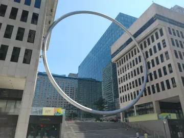 The Ring sculpture curves above a public staircase between tall city buildings.