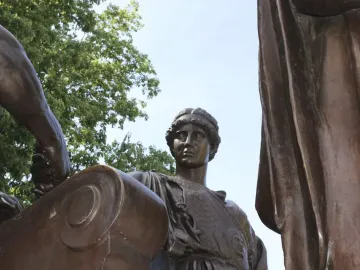 Detail of Alma Mater showing the woman’s face, braided hair, patterned bodice, and a bronze scroll with an arm resting on it.