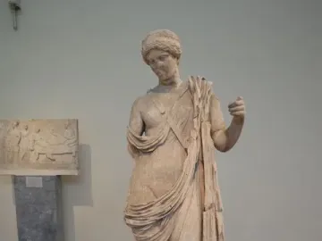 Damaged marble statue of Armed Aphrodite on a pedestal in a museum exhibit.
