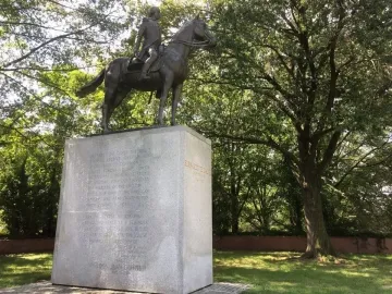 Bernardo de Gálvez equestrian statue on a tall stone pedestal surrounded by trees.