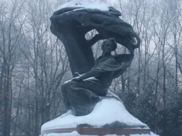 Chopin Monument in a snowy park, with a seated bronze figure beneath a large wave-like sculpture.