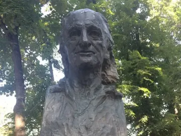 Bronze bust of Grigore Vieru on a granite pedestal in a tree-lined park.