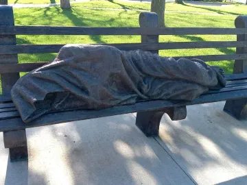 Homeless Jesus bronze sculpture of a sleeping figure on a park bench, with wounded feet exposed at one end.