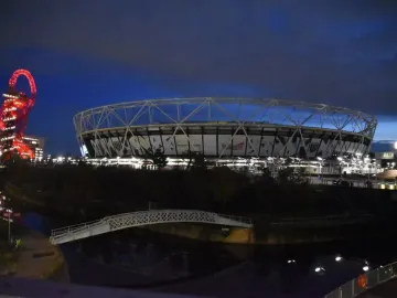 Orbit Tower glowing red beside a brightly lit stadium at dusk.