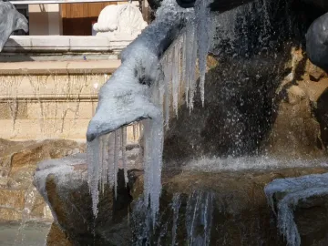 Close-up of a frozen detail on the Fontaine Bartholdi, with water flowing over stone and icicles hanging from the sculpture.