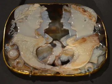 Gemma Claudia cameo with four profile portraits facing inward, gold border, and intertwined horn-shaped elements at the bottom.