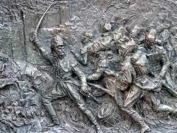 Bronze bas-relief of soldiers in battle on the José de San Martín monument, with swords, flags, and a drum in the foreground.