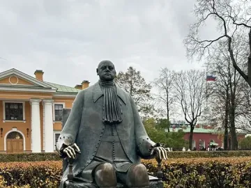 Peter I Monument shown as a bronze statue of a seated man on a stone pedestal with a low fence around it.