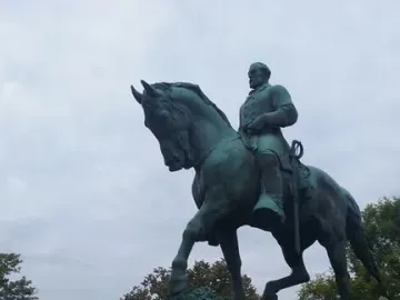 Robert E. Lee Monument showing a rider on horseback atop a tall stone pedestal with trees and cloudy sky behind it.