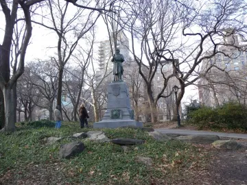 Seventh Regiment Memorial bronze figure on a stone pedestal in a winter park with city buildings behind it.
