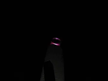 The Thanksgiving Candle monument illuminated at night, with a glowing magenta-purple ring at the top.