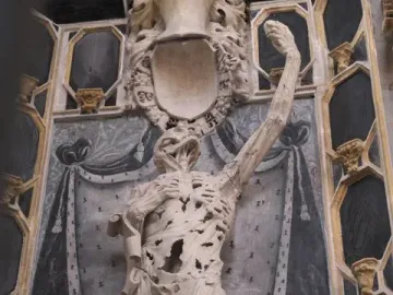 Transi of René of Chalon, an emaciated stone figure holding a heart to its chest in a dark niche.
