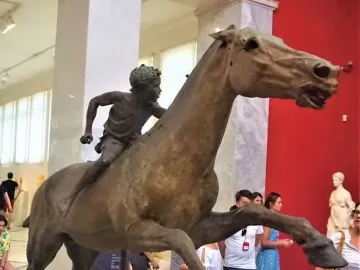 Jockey of Artemision bronze sculpture showing a young rider leaning forward on a horse in motion inside a museum.