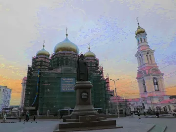 Monument to Dimitry of Rostov on a tiered pedestal in a square, with a scaffolded church, bell tower, and sunset sky behind it.