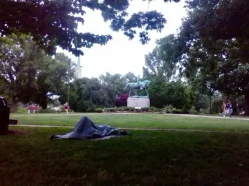 Robert E. Lee Monument in a park, with a person lying wrapped in a blanket on the grass in the foreground.