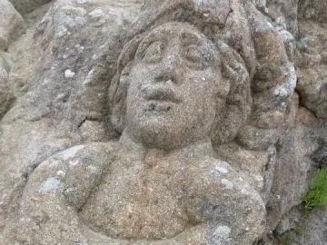 Carved figure in the Rothéneuf Sculpted Rocks, with a prominent face and arms crossed over the chest in a rough rock surface.