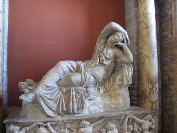 Sleeping Ariadne marble sculpture reclining against a reddish wall with ornate columns nearby.