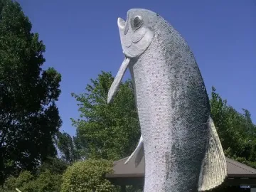 The Big Trout sculpture standing in a circular pool with trees and a gazebo nearby.