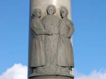 Electio Viritim Monument with a bronze relief of three figures on a tall light-grey column.