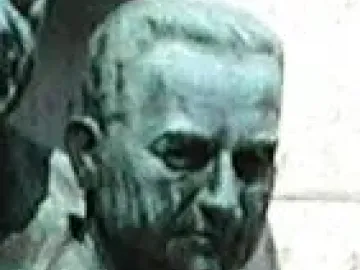 Bronze bust of Joseph L. Melnick with a green patina, shown in close-up against a pale wall.