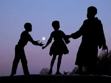 Silhouetted figures stand against a purple-blue sky with the moon between them.