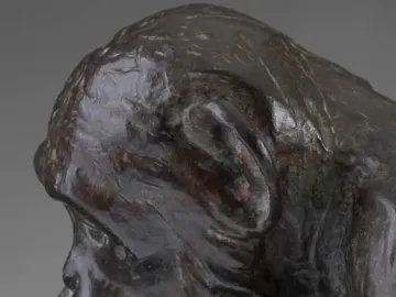 Bronze sculpture of a chimpanzee holding a human skull while seated on books, including one labeled Darwin.