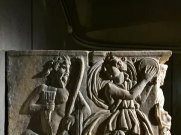 Roman marble relief from the Sarcophagus of the Triumph of Bacchus showing a bearded satyr-like figure playing panpipes beside a dancing woman with a tambourine and a serpent emerging from a vessel.