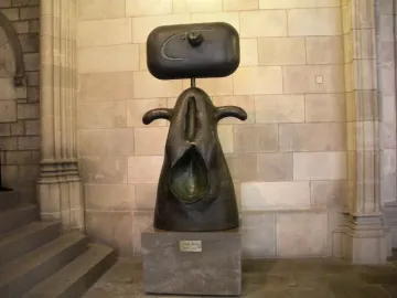 Femme, a dark abstract sculpture with a rectangular head-like top and curved forms, displayed on a stone pedestal indoors.