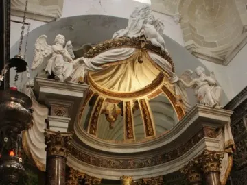 Crowned white marble Madonna di Trapani statue with the infant Jesus on an ornate altar with flowers and candles.