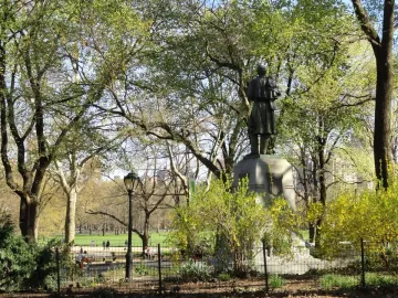 Seventh Regiment Memorial statue on a tall stone pedestal in Central Park, seen from behind among trees and shrubs.