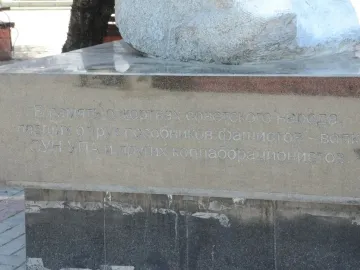 Stone base of The Shot in the Back monument with a Cyrillic inscription and a partially visible stone sculpture above it.