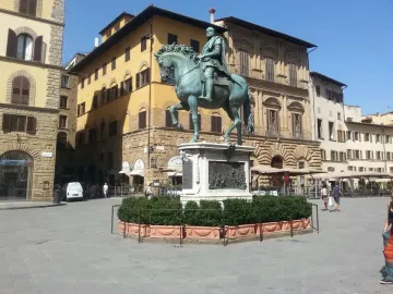 Cosimo I equestrian monument on a tall stone pedestal in a city square, with historic buildings and a few people nearby.