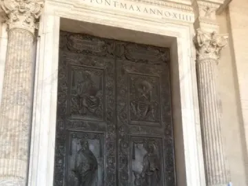 The Filarete Door with dark bronze relief panels framed by marble columns, with people passing in front.