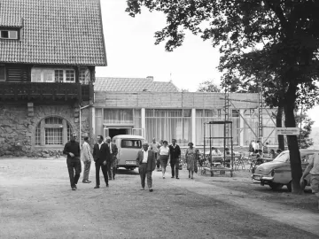 Crowds gather beside buildings on the plateau below the Kyffhäuser Monument, including a stone building and a modern café terrace.