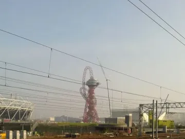 Orbit Tower rising behind railway tracks and overhead wires, with part of a stadium visible to the left.
