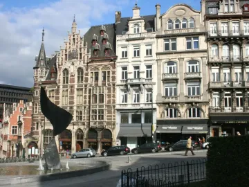The Whirling Ear sculpture rises from a fountain, with historic buildings behind it on a city street.