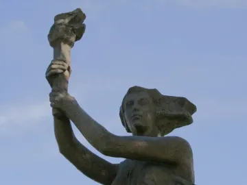 Victims of Communism Memorial statue of a female figure holding a torch aloft against a blue sky.